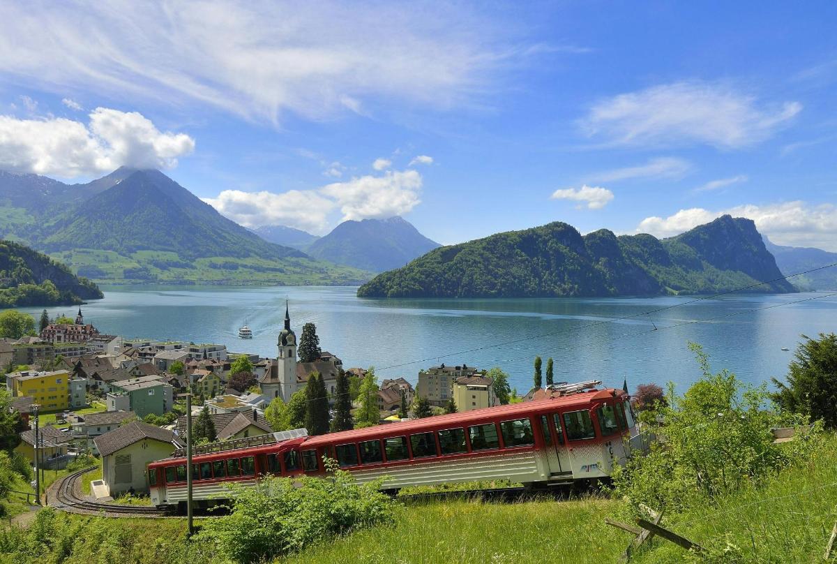 a red and white train traveling past a town next to a lake