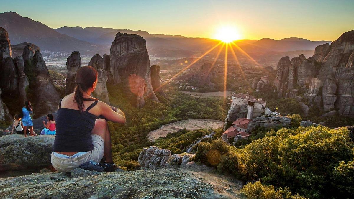 a woman sitting on top of a mountain watching the sunset