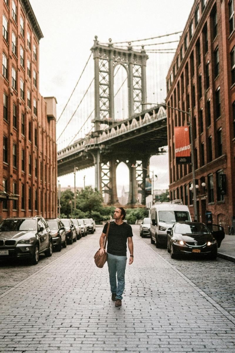 a man walking down a street in front of a bridge