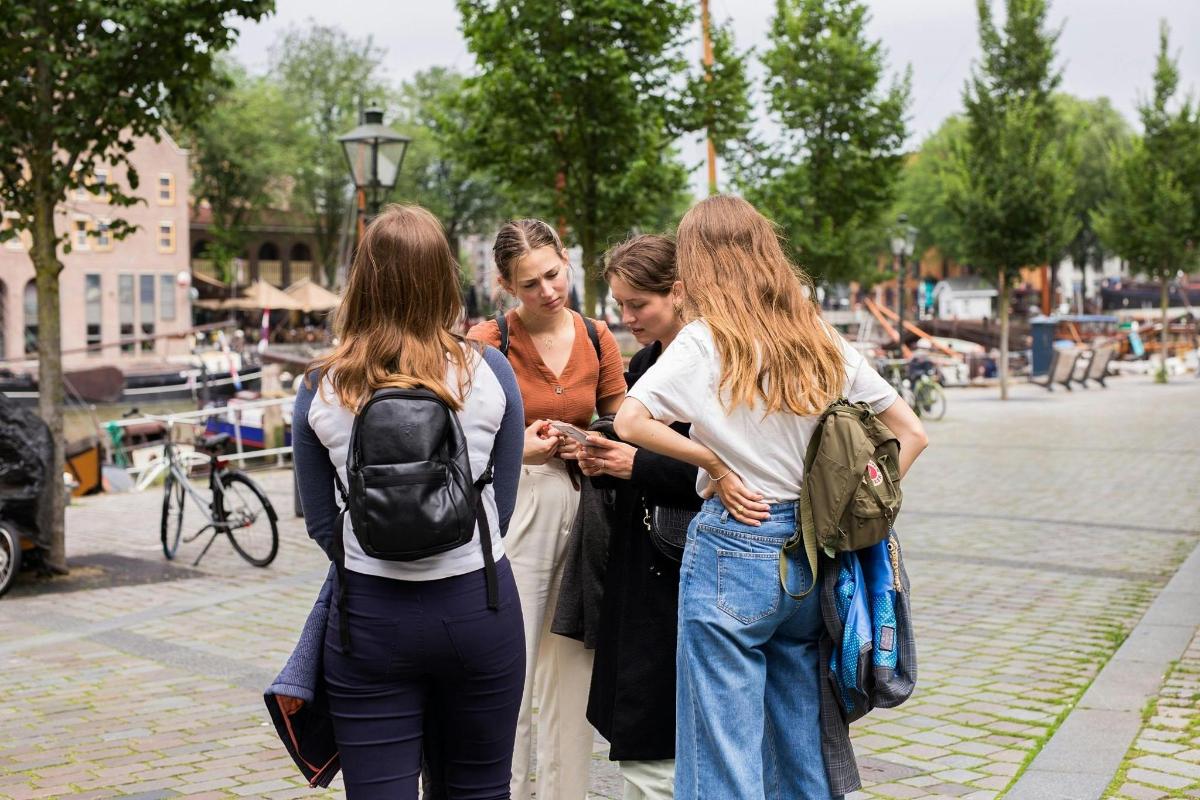 a group of women standing on a sidewalk looking at a cell phone