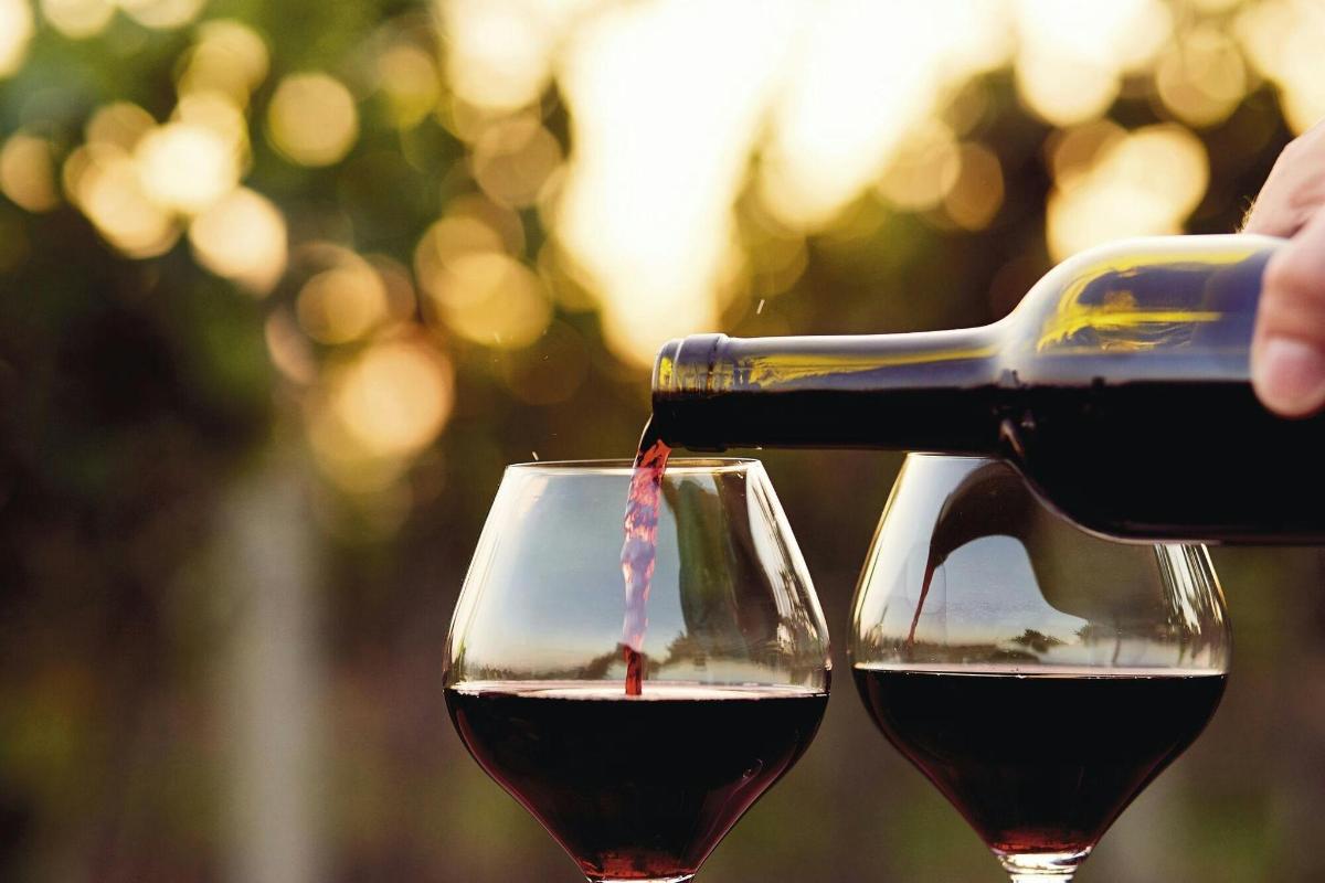a person pouring red wine into two wine glasses
