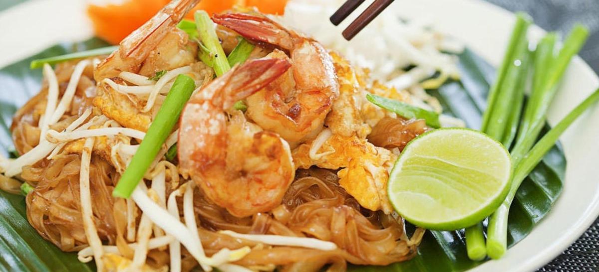 a plate of noodles with shrimp and a lime