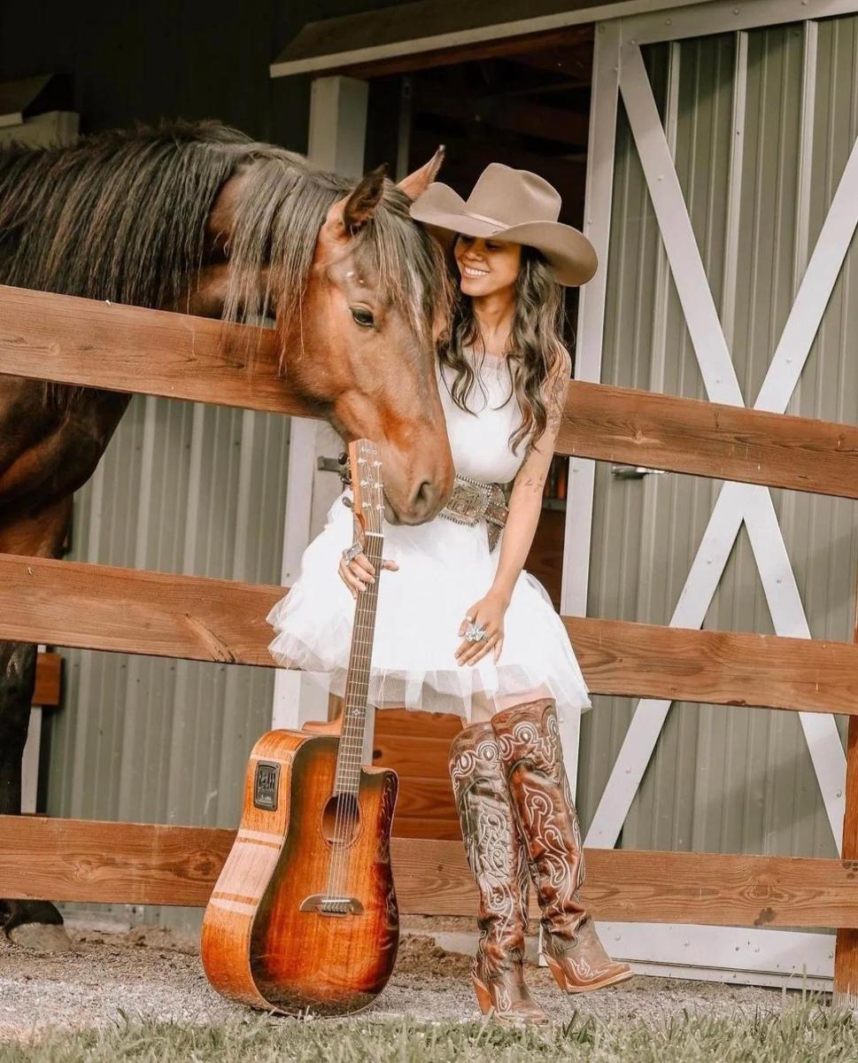a woman in a cowboy hat with a guitar and a horse