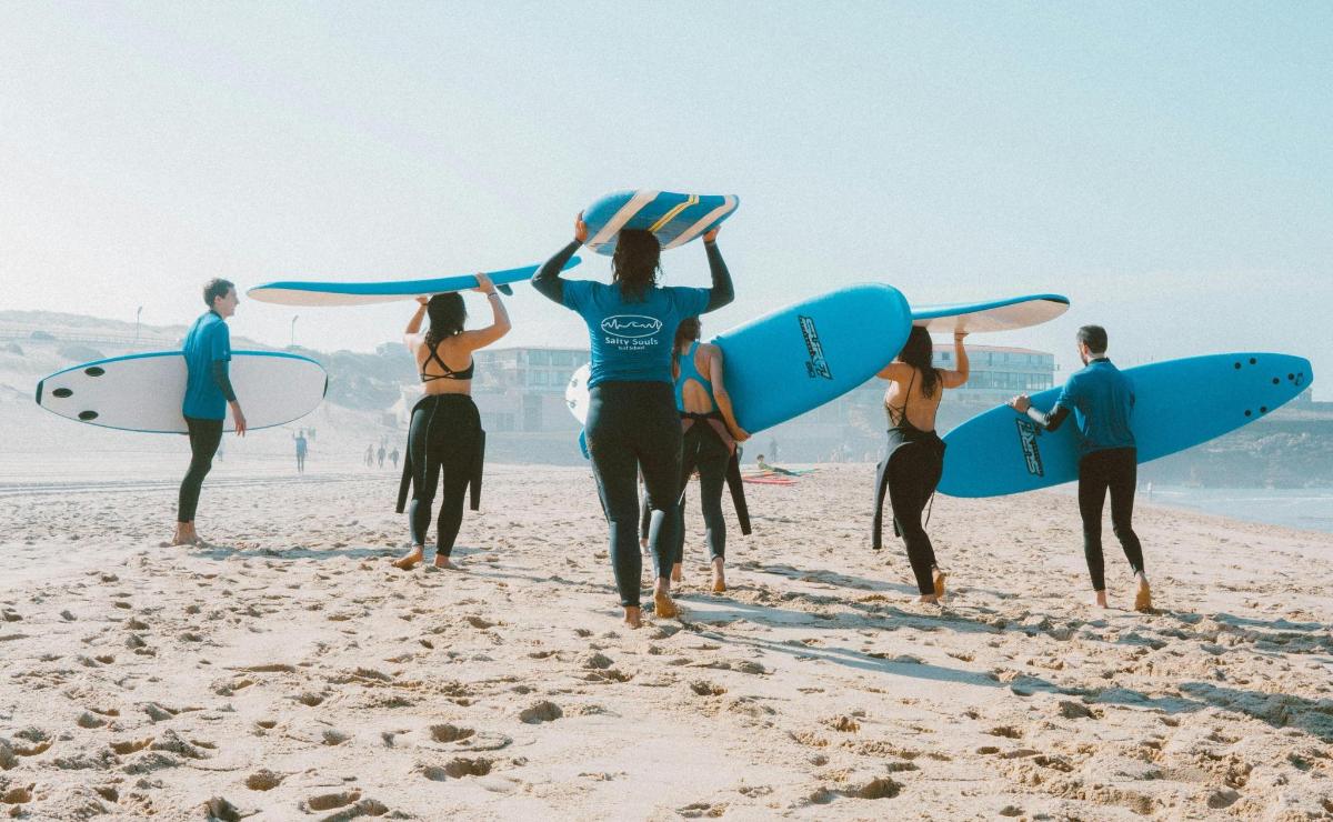a group of people walking on the beach with surfboards