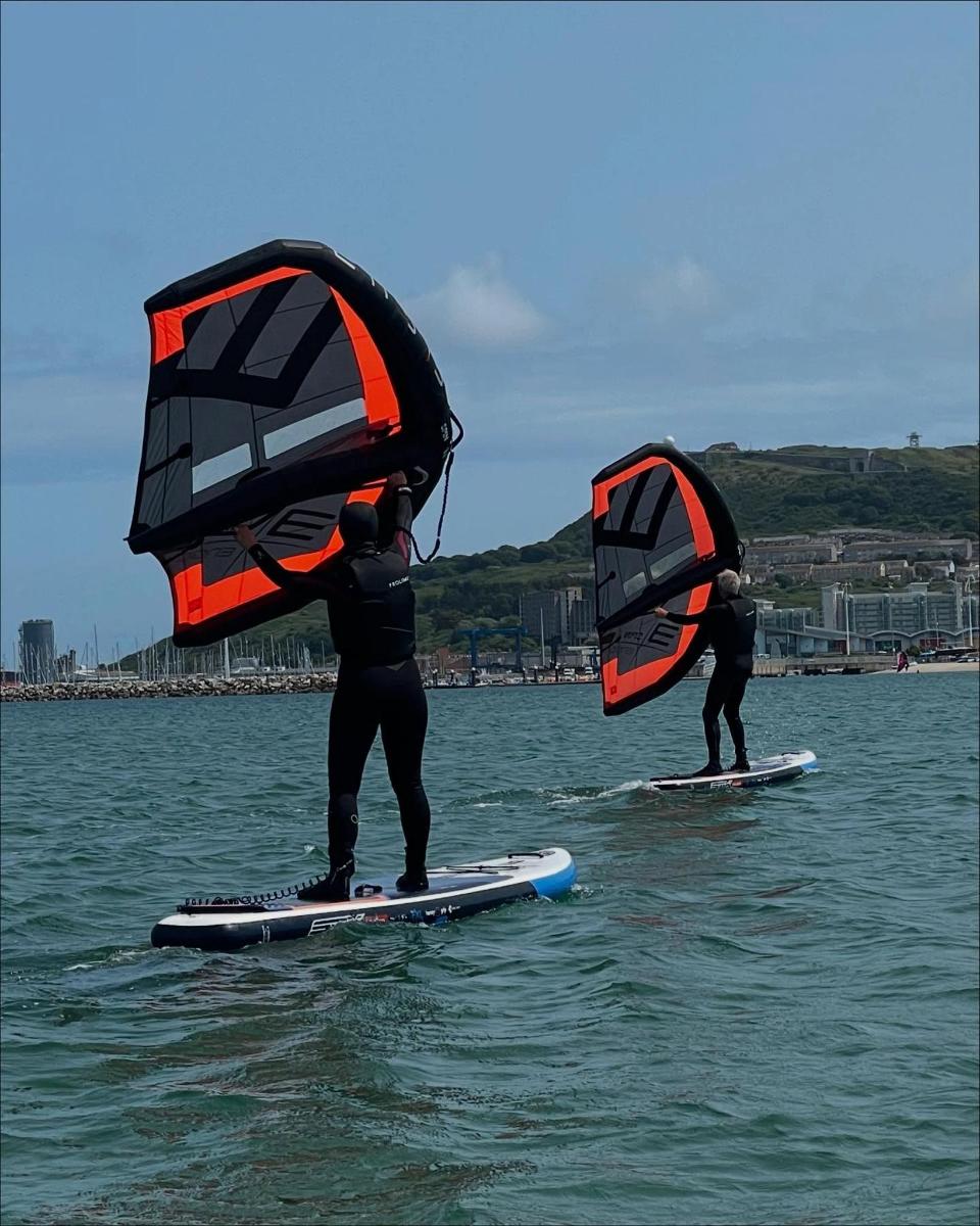 two people on surfboards in the water holding sails