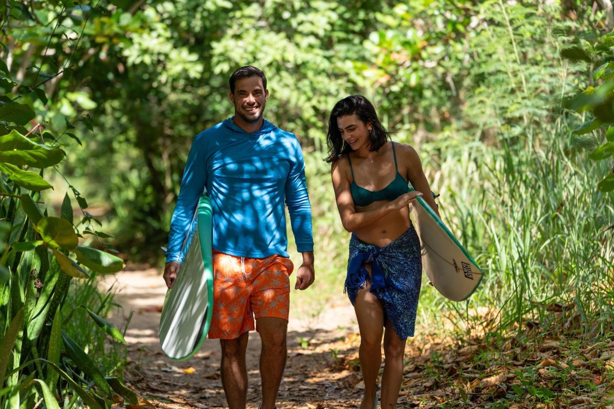 a man and a woman walking down a path with surfboards