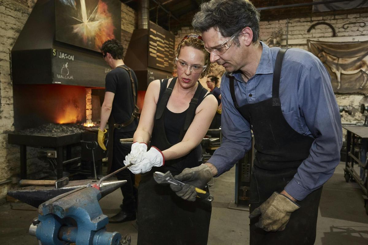 a man and a woman standing in a workshop cutting avil